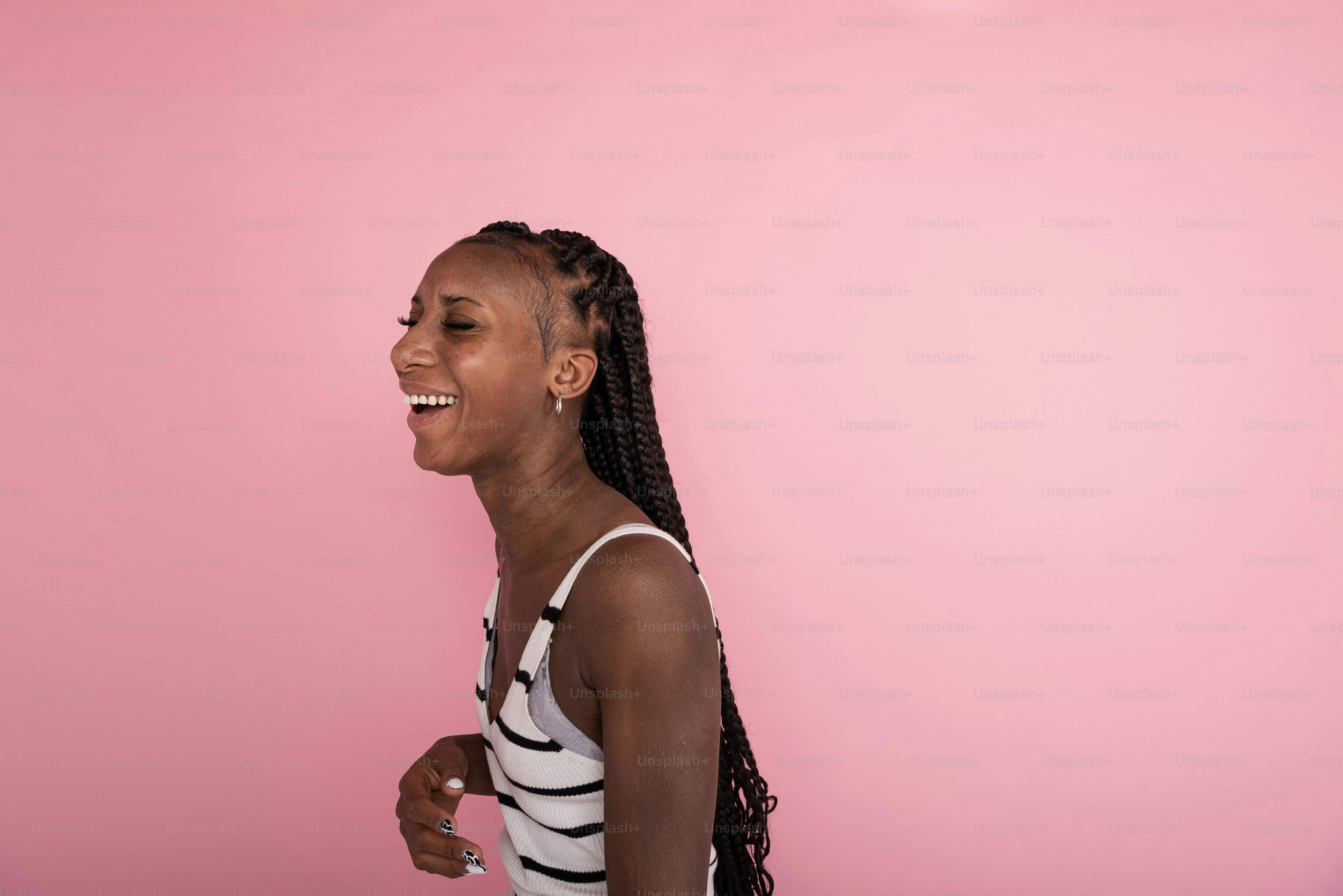 a woman with braids laughing against a pink background