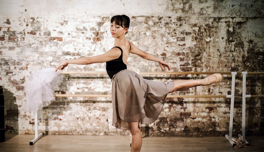 a woman in a black top and tan skirt is doing a ballet pose