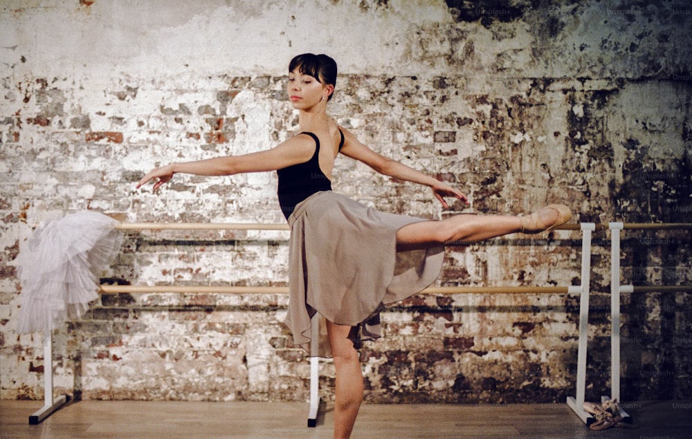 a woman in a black top and tan skirt is doing a ballet pose