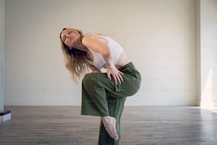 a woman in a white tank top is doing a yoga pose