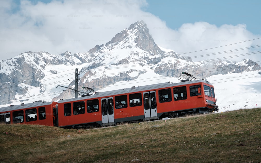 a red train traveling past a snow covered mountain