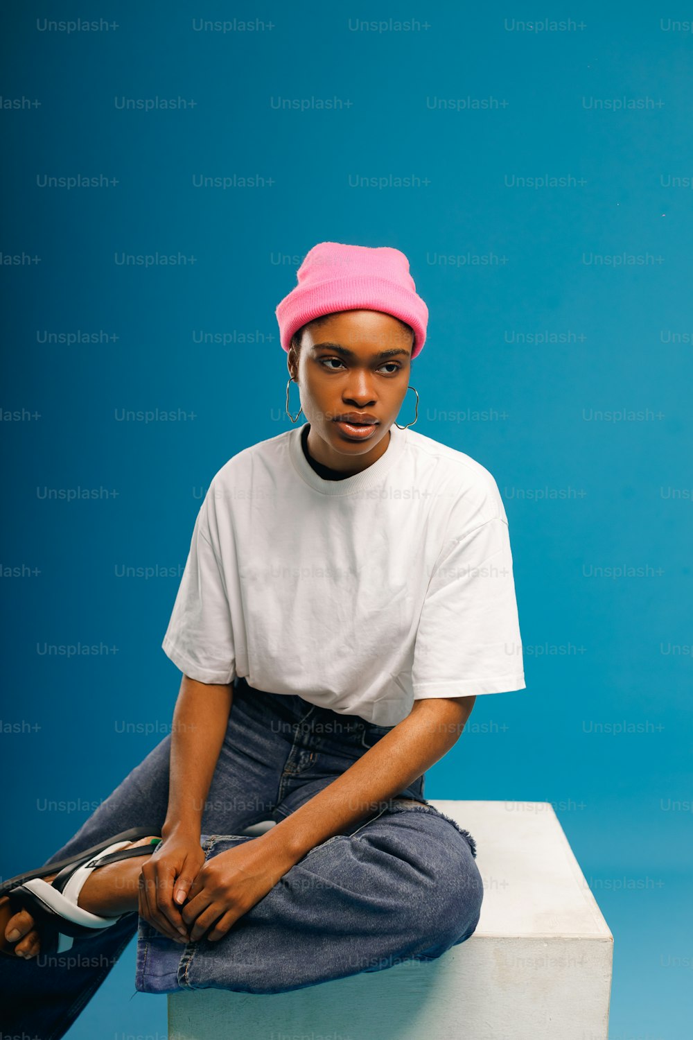 Une femme assise au sommet d’un bloc blanc portant un chapeau rose