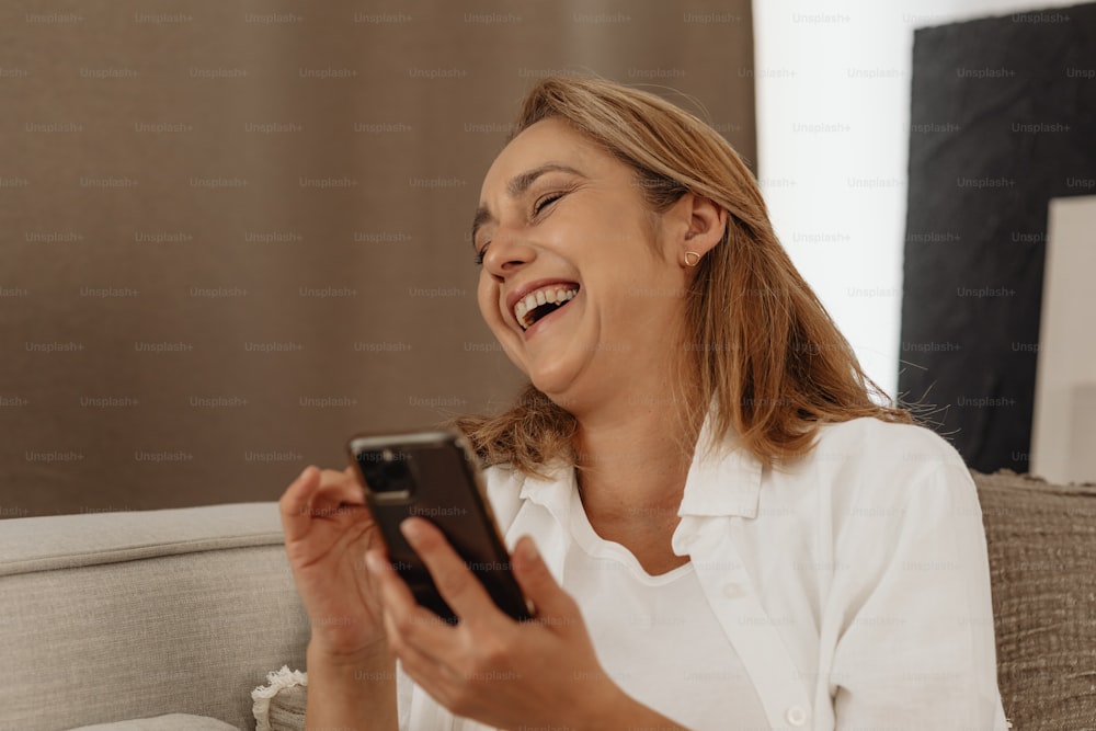 Una mujer riendo mientras mira un teléfono celular