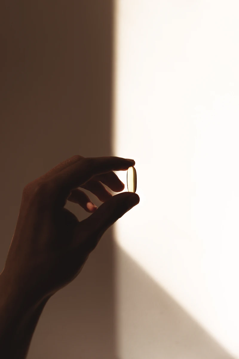 Hand mit Kapsel vor heller Wand — Nahrungsergänzung
