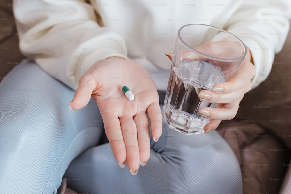 Una mujer sosteniendo un vaso de agua y una pastilla