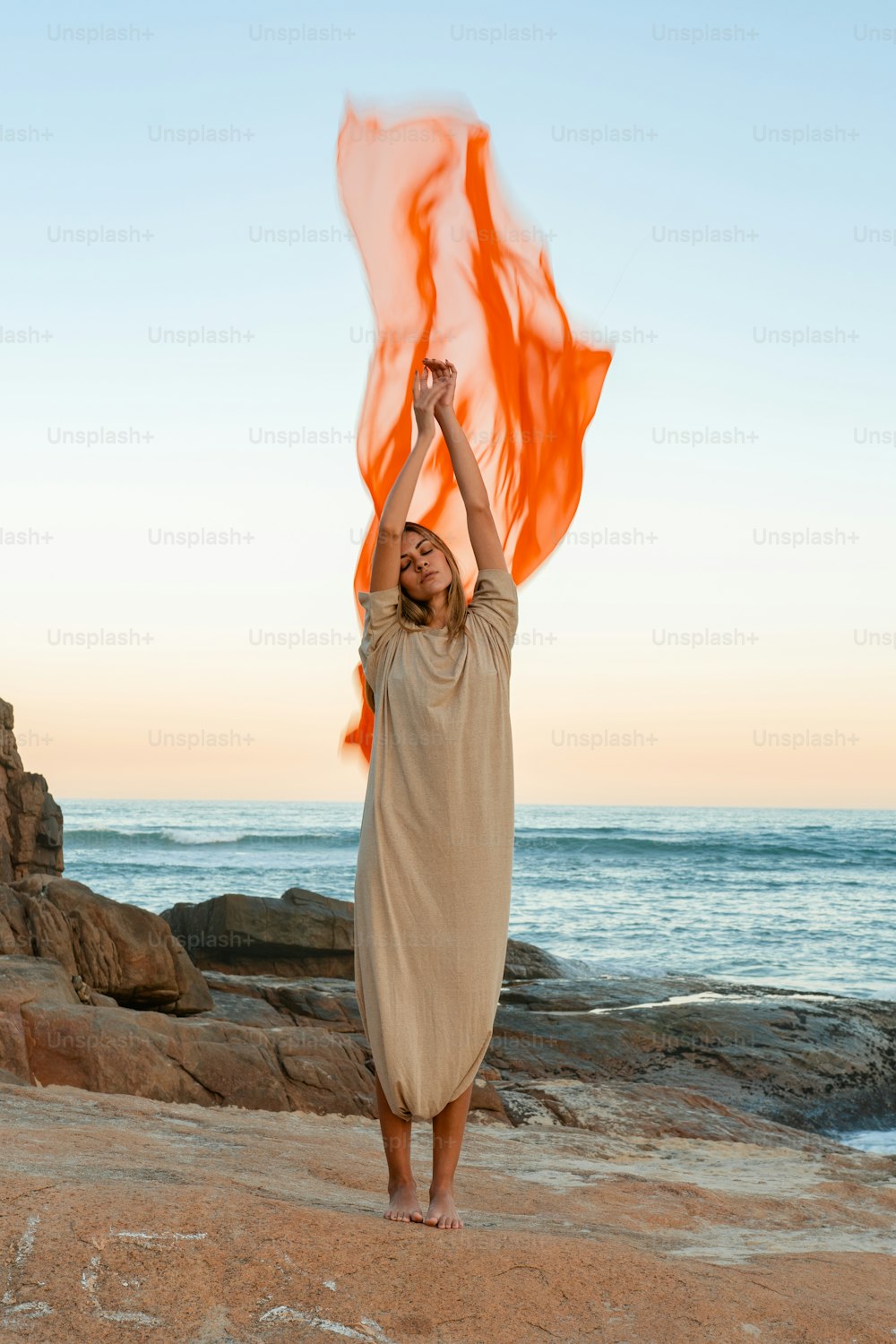 a woman standing on top of a beach holding an orange scarf