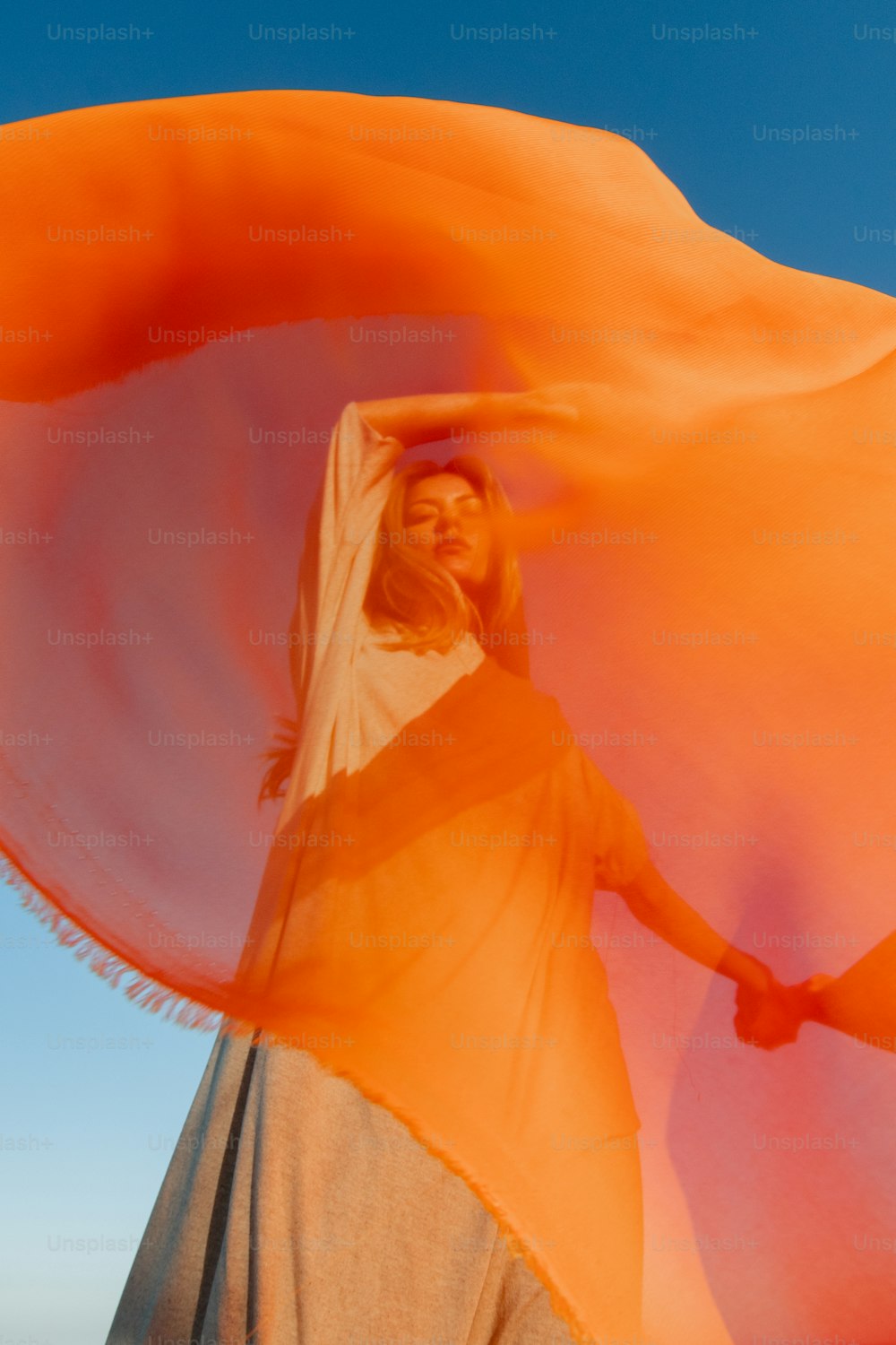 a woman is holding a large orange scarf