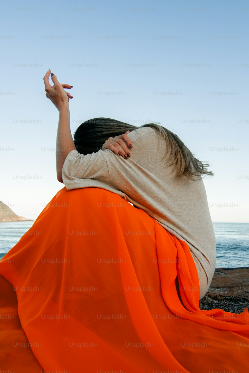 eine frau in einem orangefarbenen kleid, die an einem strand sitzt