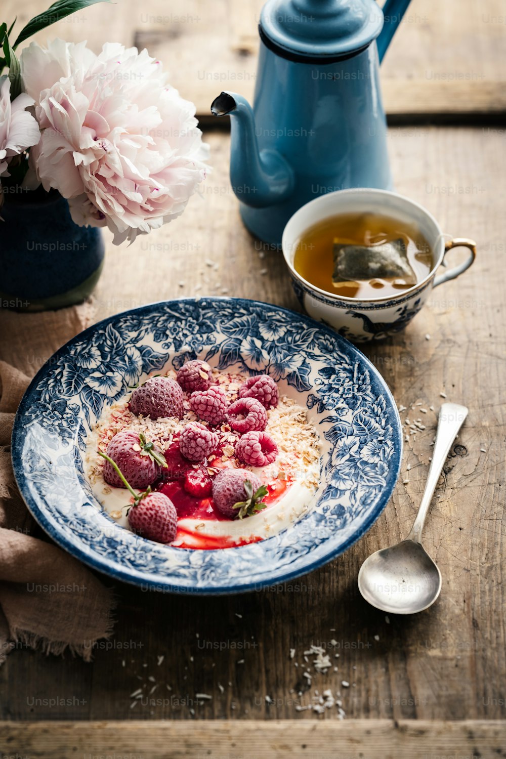 a bowl of yogurt with raspberries and a cup of tea