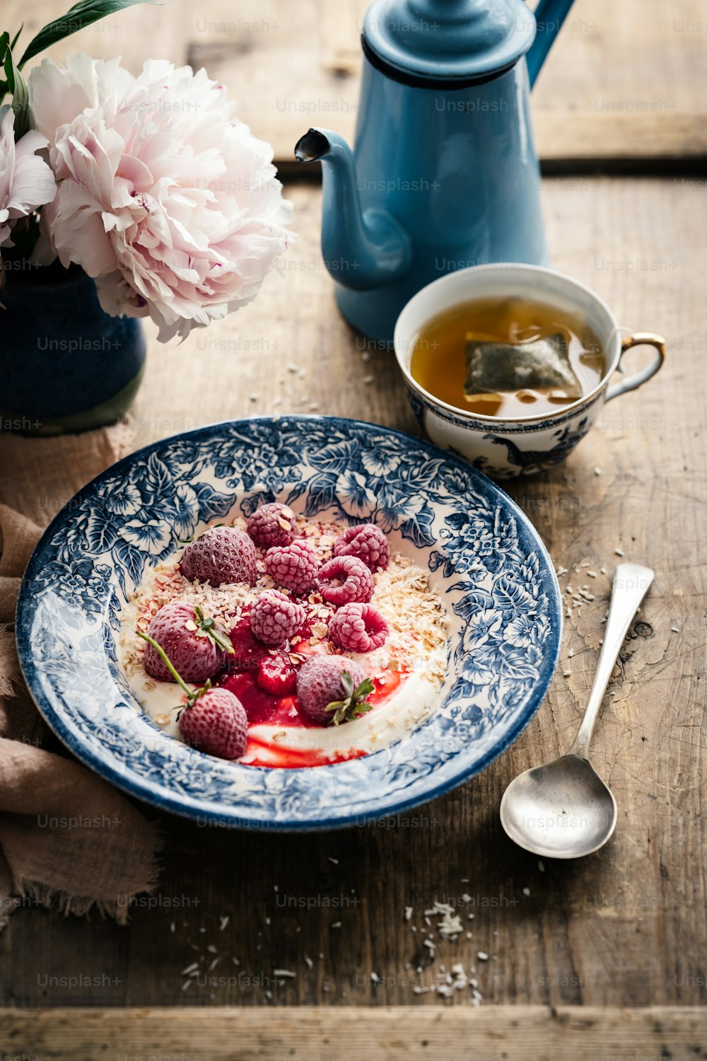 un bol de yogourt avec des framboises et une tasse de thé