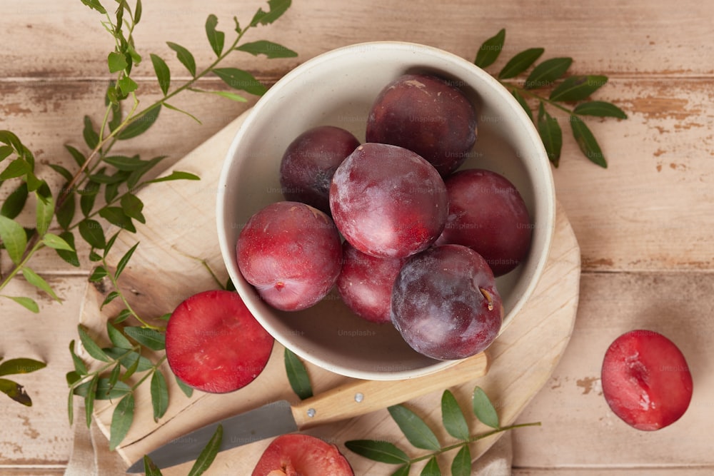 a bowl of plums on a cutting board with a knife