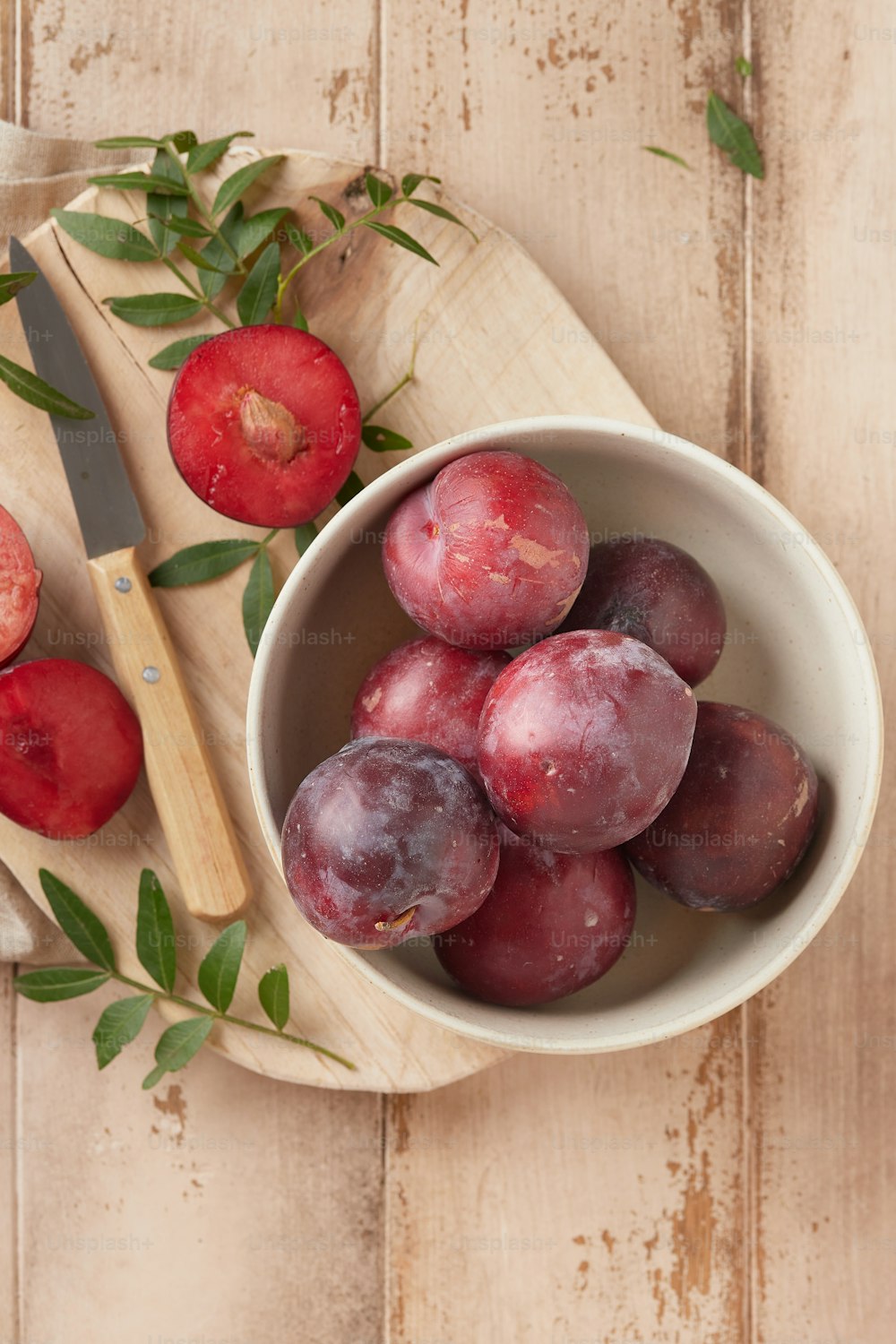 a bowl of plums and a knife on a wooden table