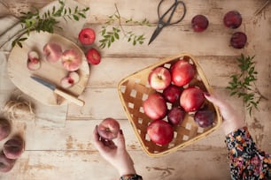 uma pessoa segurando uma cesta de maçãs em uma mesa
