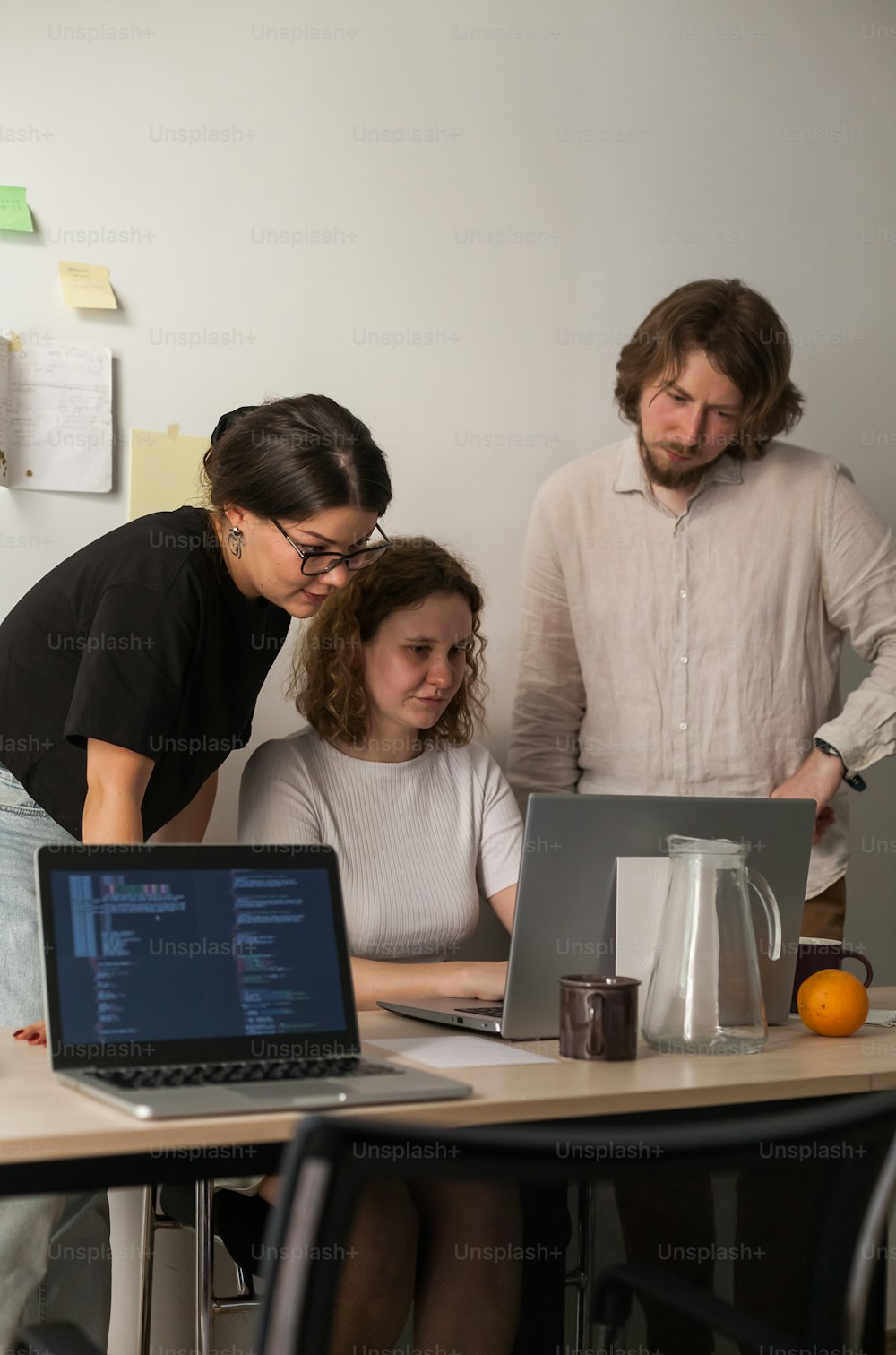 a group of people standing around a table with laptops