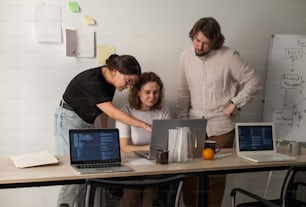 a group of people standing around a table with laptops