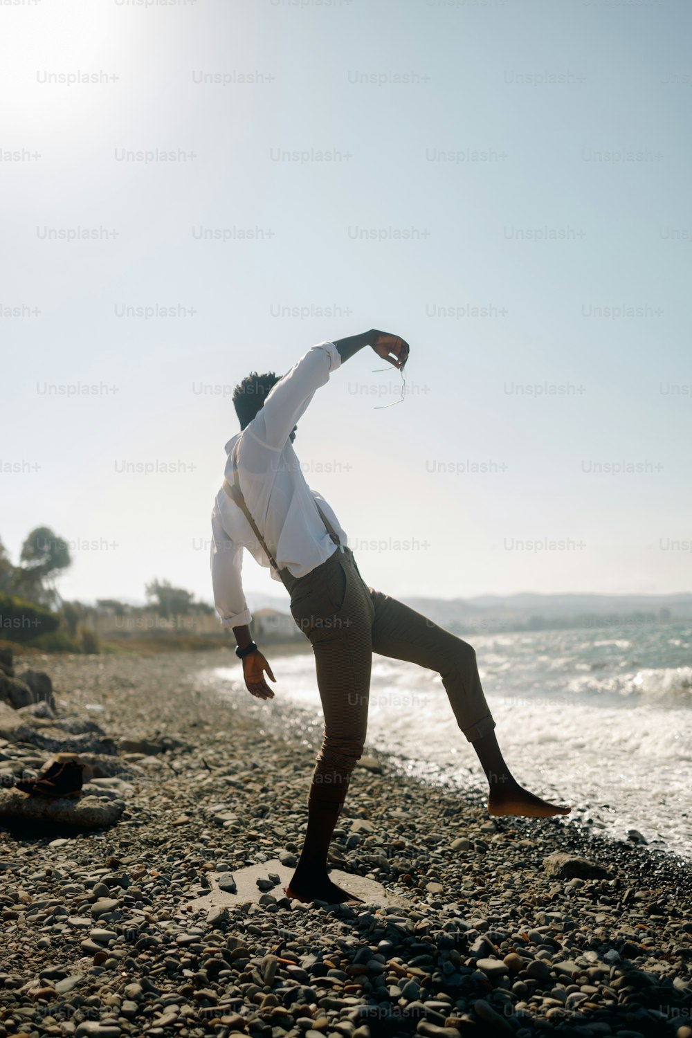 a man in a white shirt doing a yoga pose on the beach