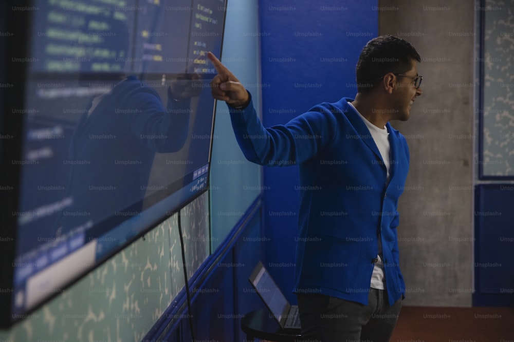 a man in a blue jacket points at a computer screen