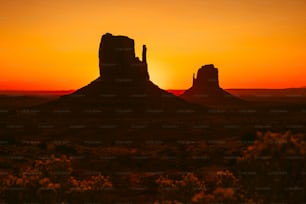 El sol se está poniendo sobre el desierto con una formación rocosa en primer plano