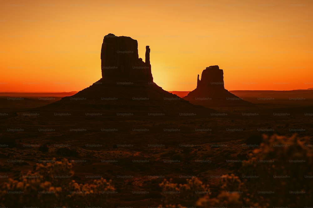 太陽は前景に岩層で砂漠に沈んでいます