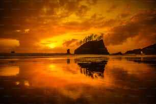 the sun is setting over a beach with a rock formation