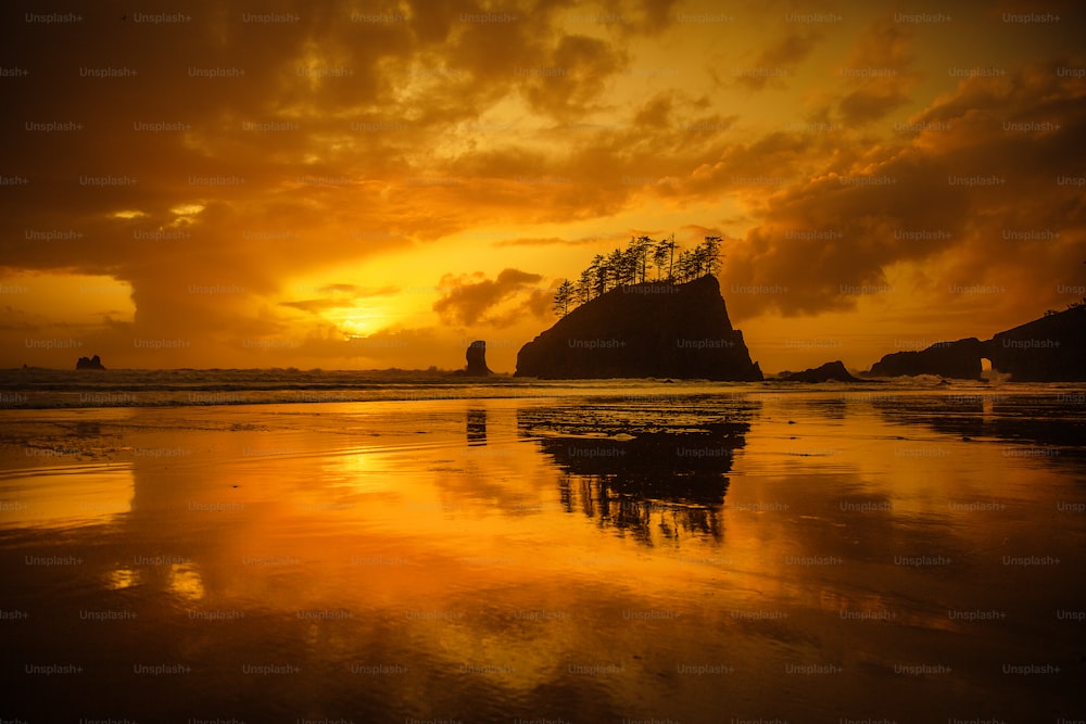 the sun is setting over a beach with a rock formation