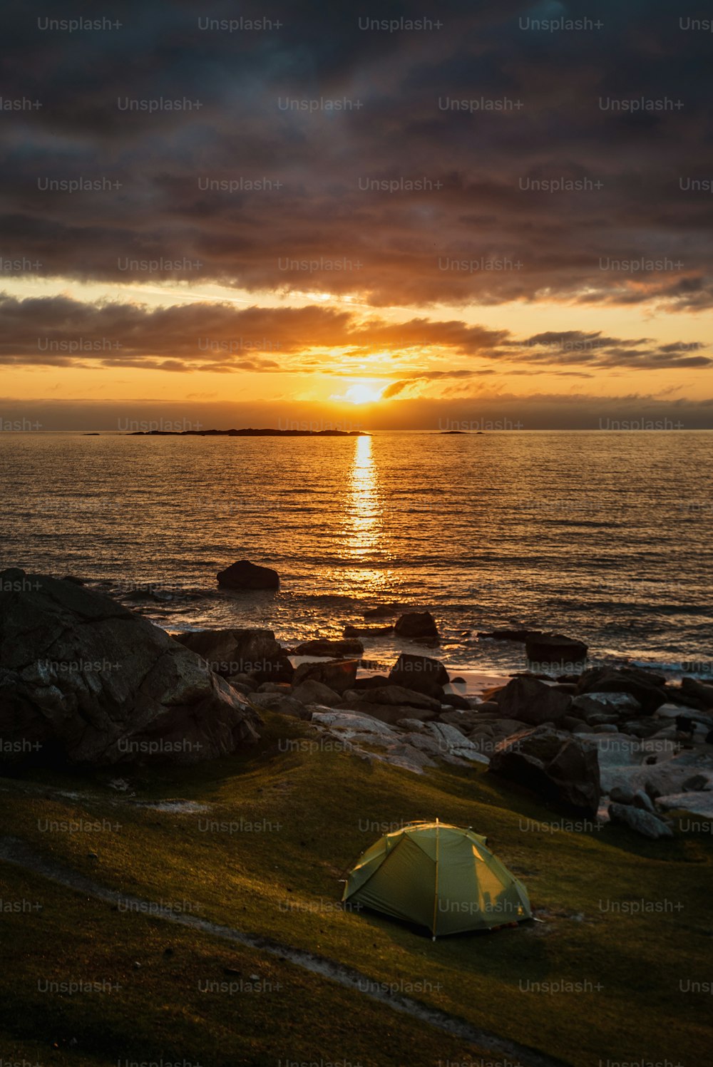 a tent is set up on a rocky beach at sunset