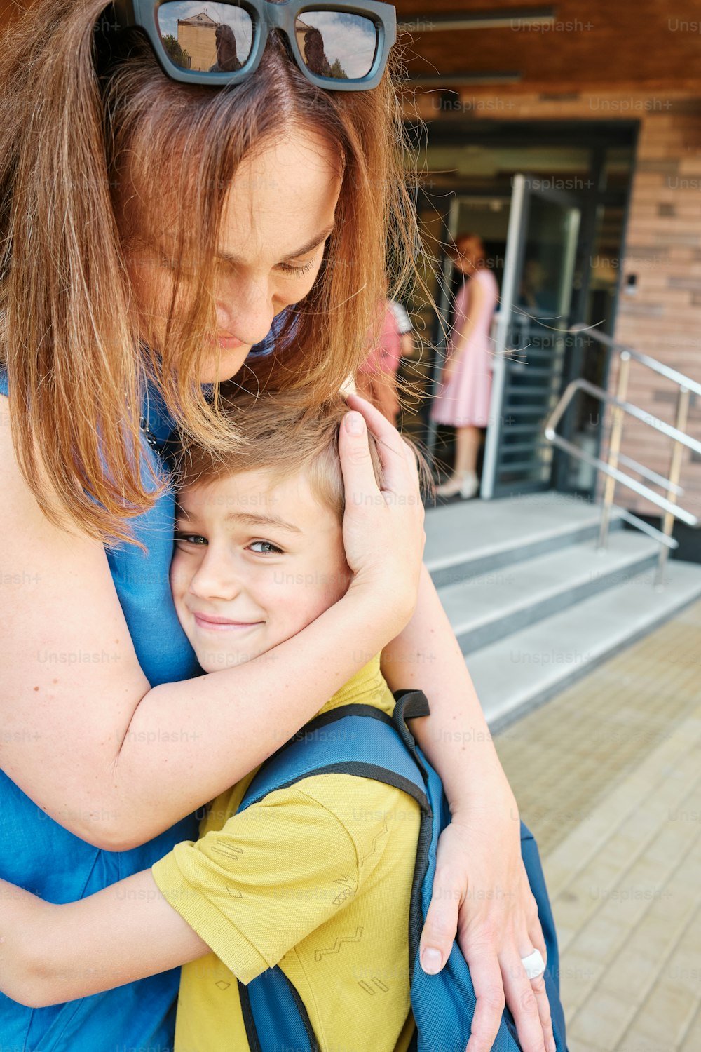 a woman is hugging a young boy in front of a building