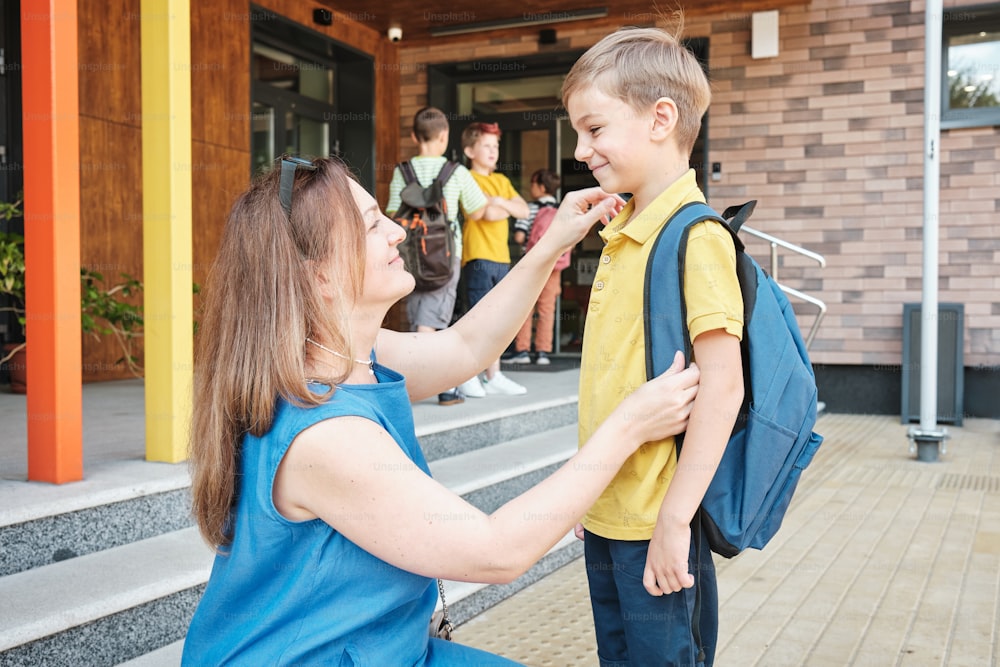 a woman helping a young boy with his backpack