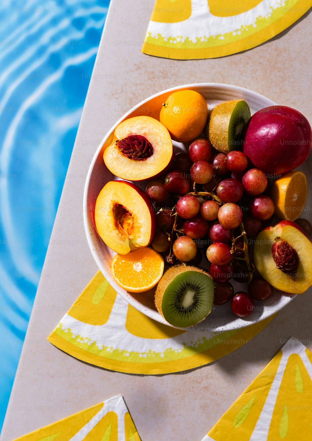 uma tigela de frutas sentada em cima de uma mesa ao lado de uma piscina