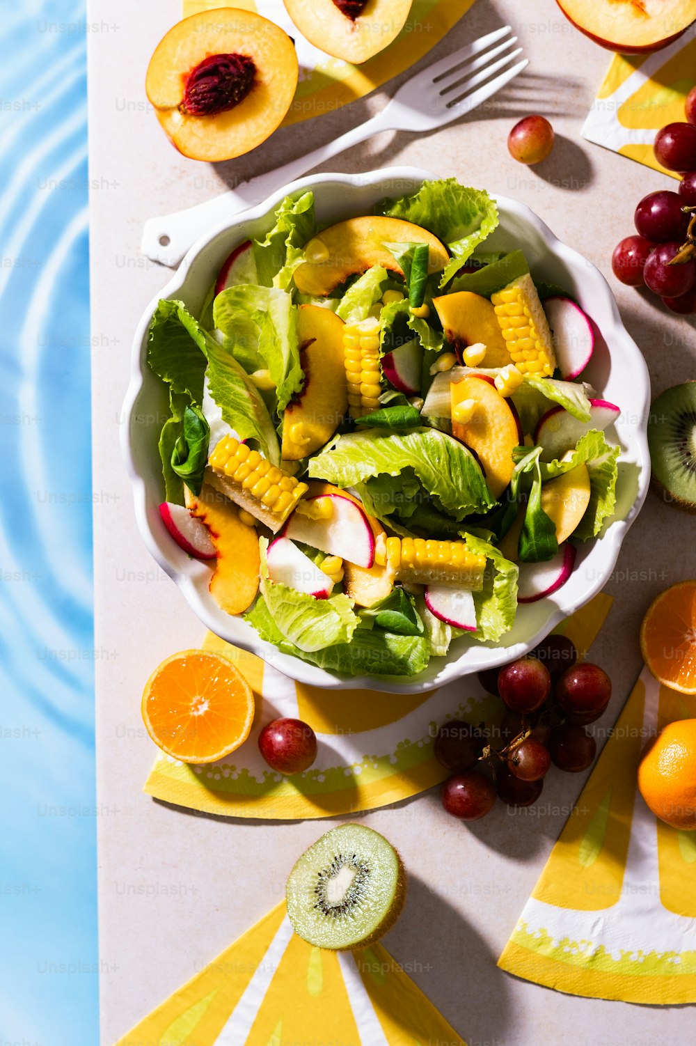 a white bowl filled with a salad next to sliced fruit