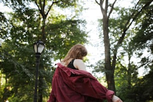 a woman in a red cape walking through a park