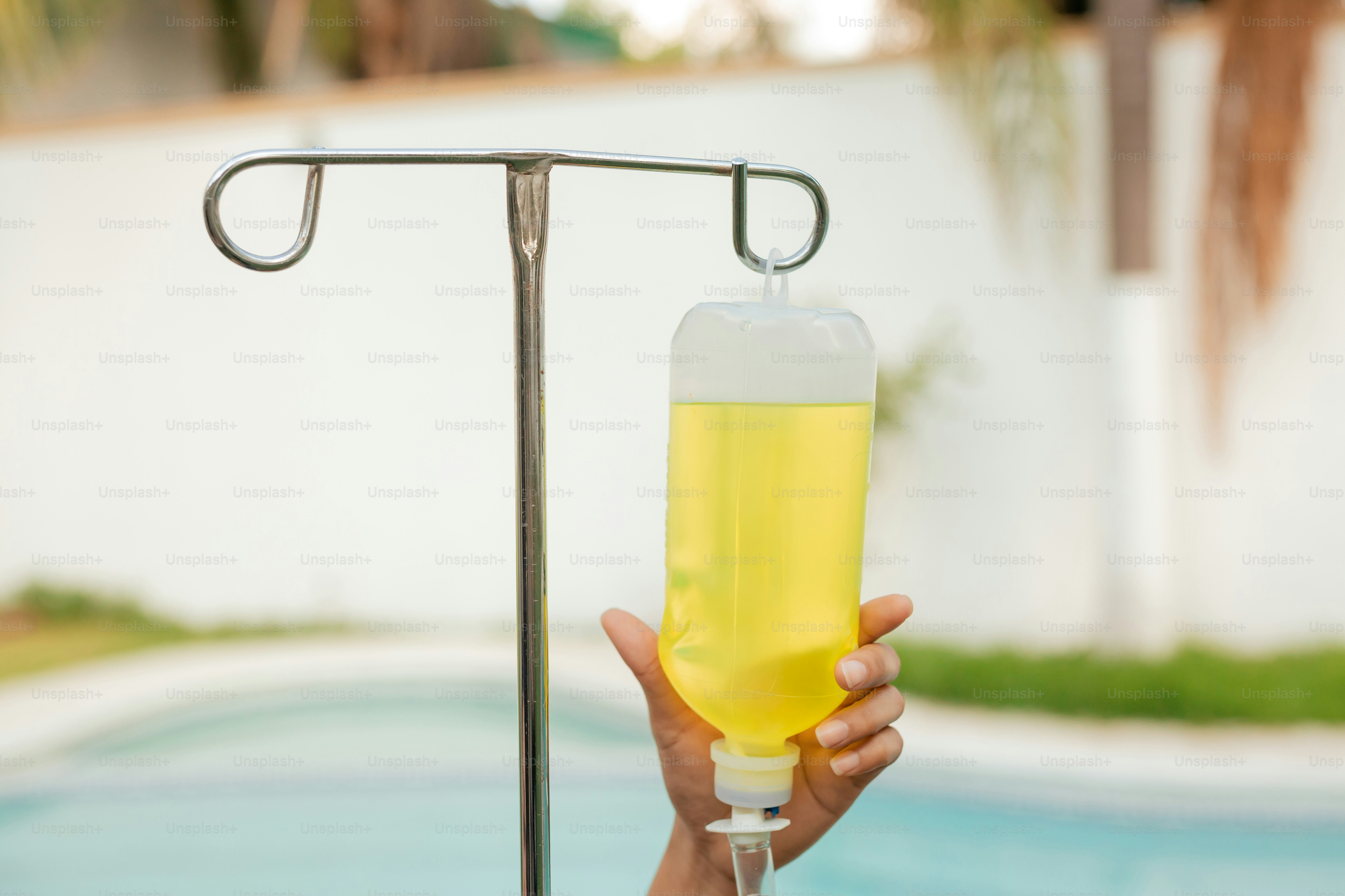 a person holding a bottle of liquid in front of a swimming pool