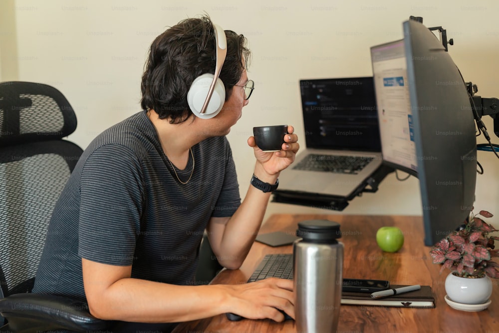 Un hombre sentado frente a una computadora sosteniendo una taza de café