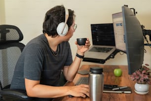 a man sitting in front of a computer holding a cup of coffee