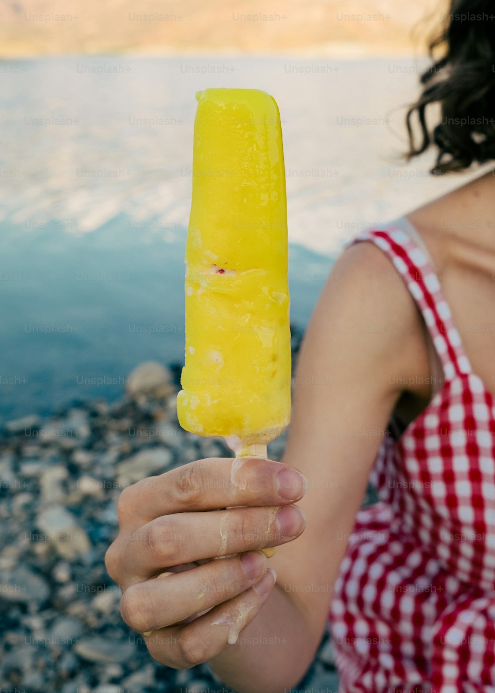 a woman in a red and white checkered dress holding a yellow popsicle