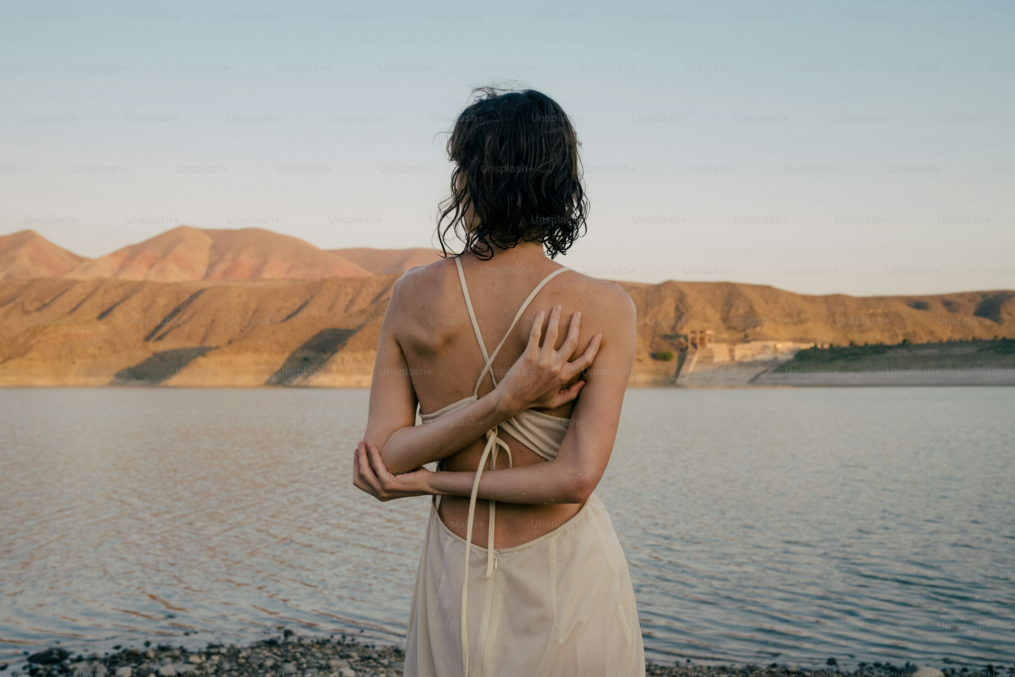 A woman standing on a beach next to a body of water photo – Woman Image ...