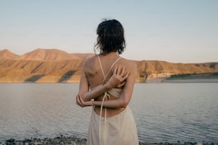 Una mujer parada en una playa junto a un cuerpo de agua