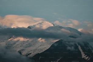 a snowy mountain covered in clouds under a blue sky