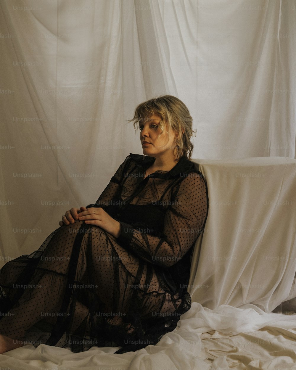 a woman sitting on a bed in a sheer dress