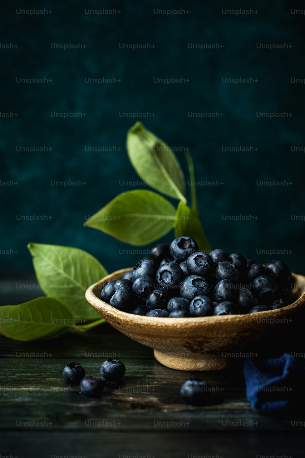 a wooden bowl filled with blueberries next to a green leaf