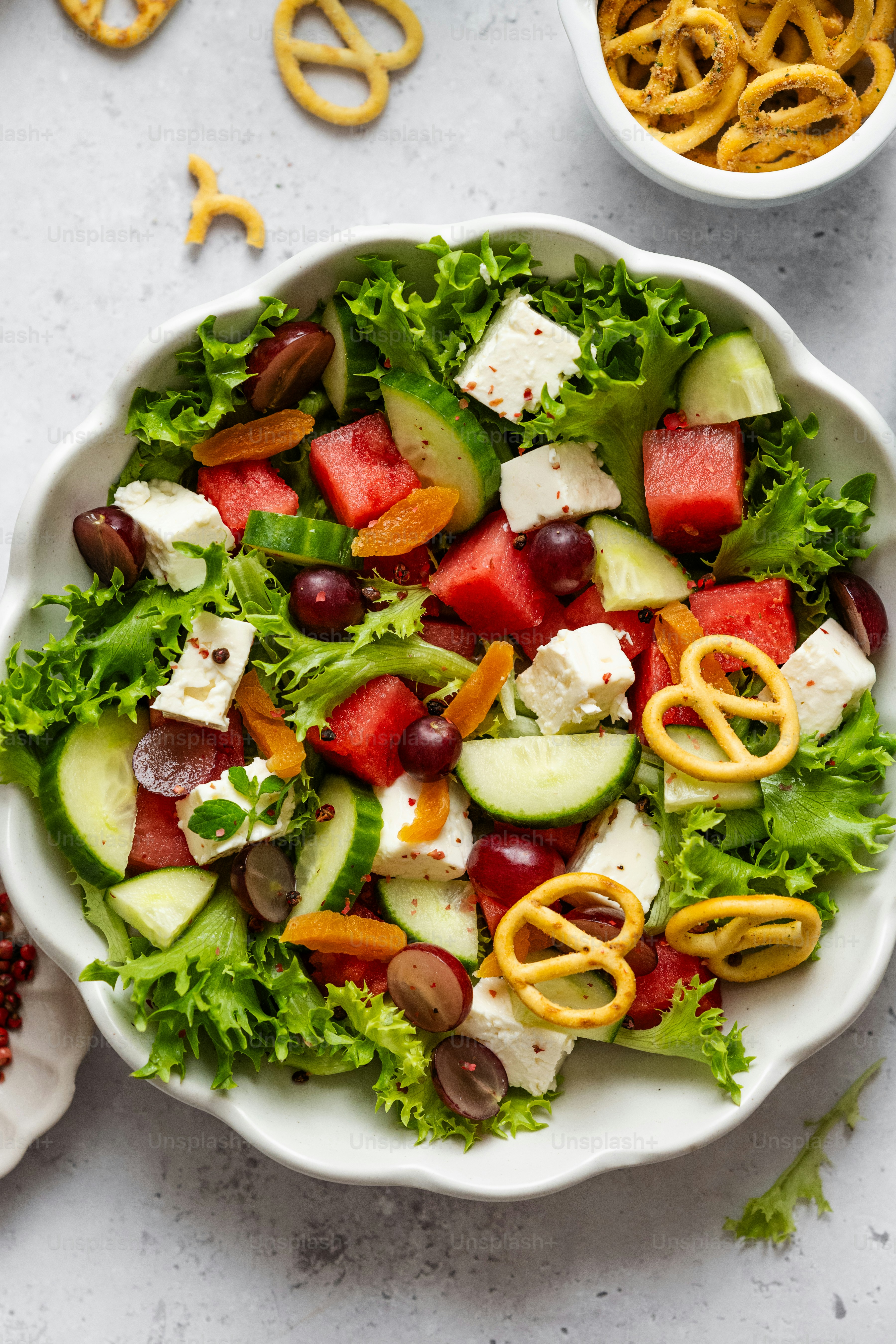 A white bowl filled with a salad next to a bowl of pretzels photo