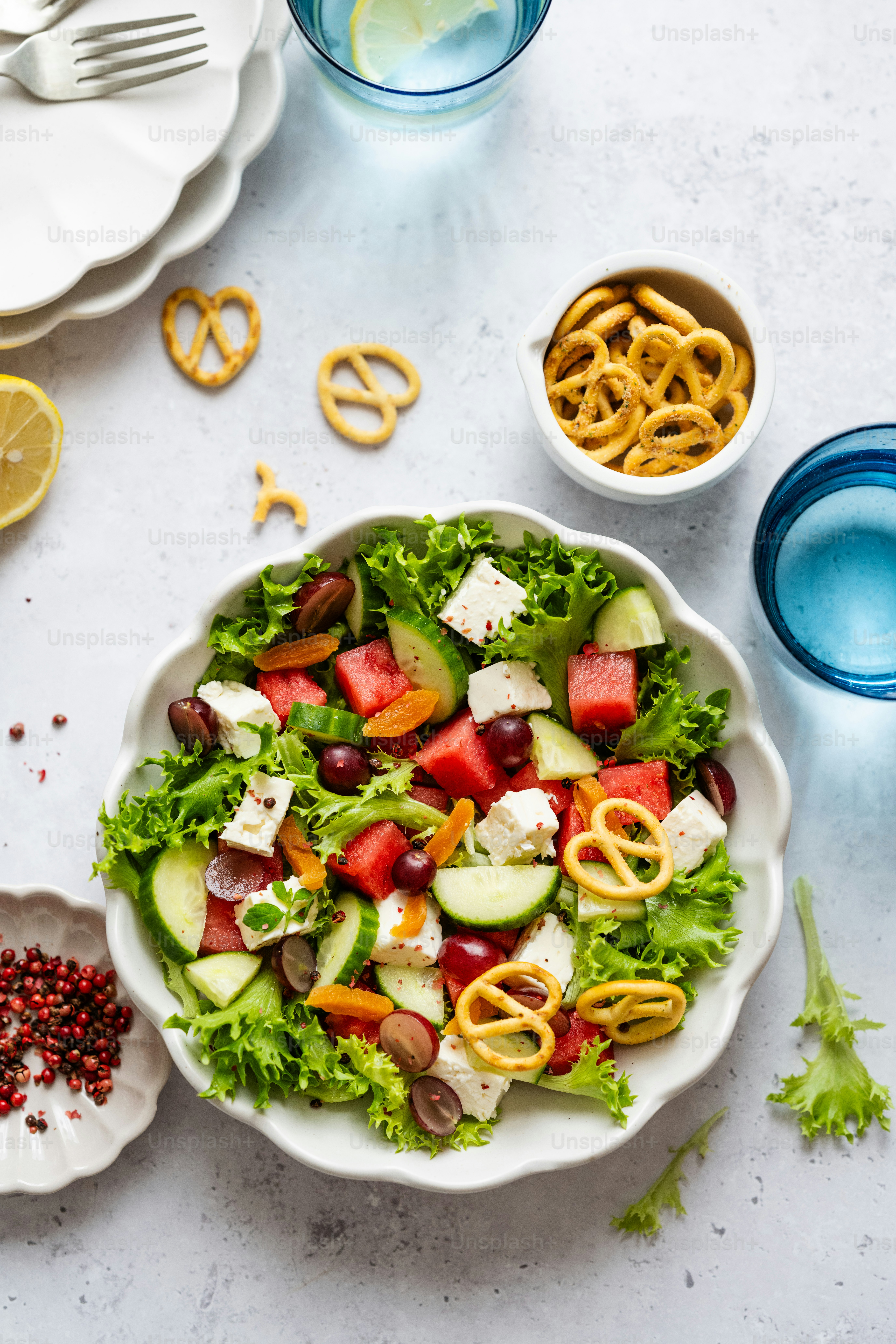 Un tazón blanco lleno de una ensalada junto a un tazón de pretzels