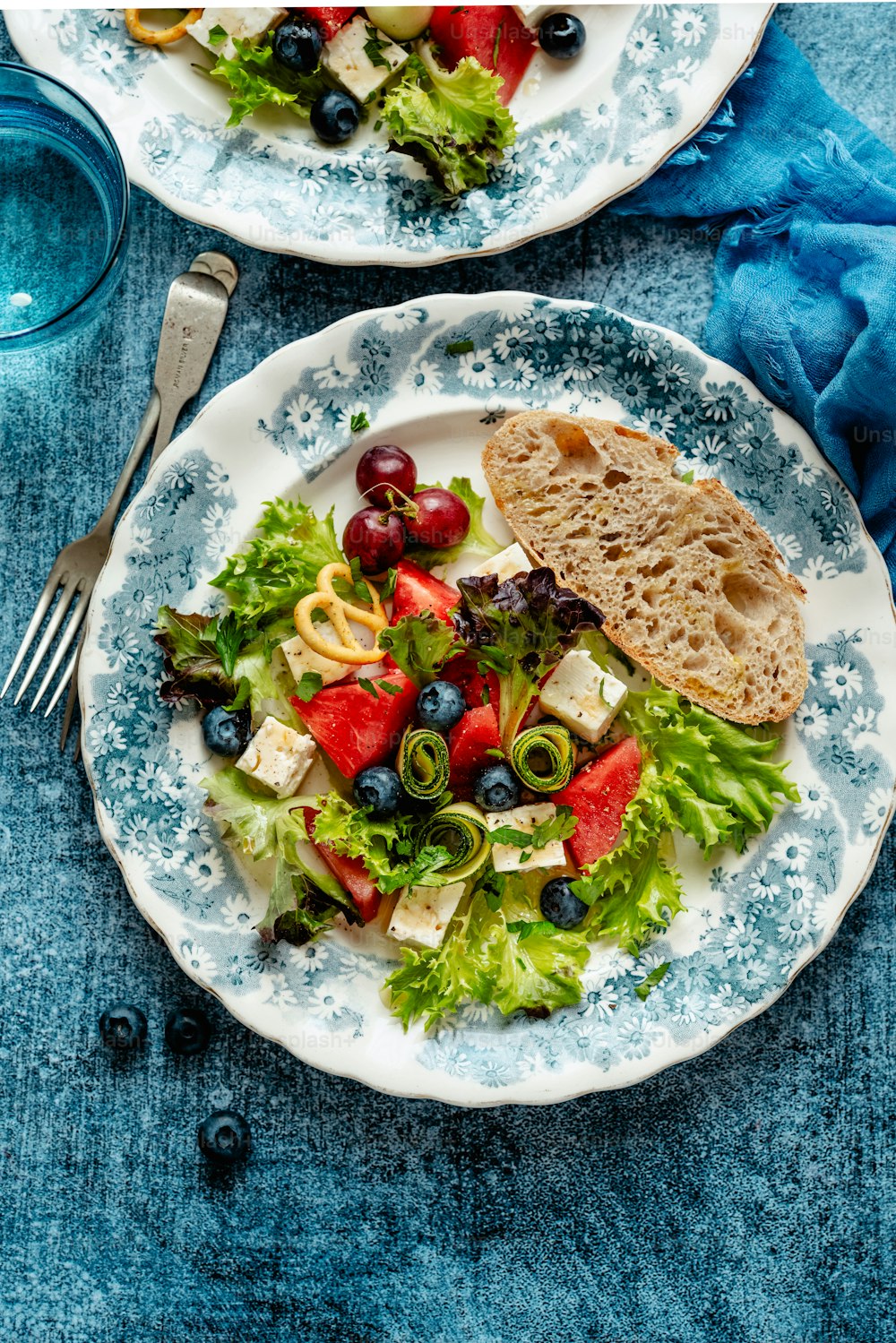 two plates of salad with bread and blueberries