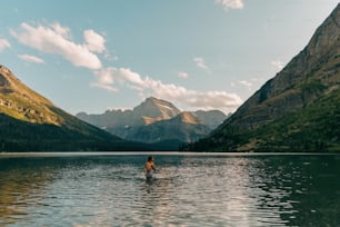 une personne pataugeant dans un lac avec des montagnes en arrière-plan
