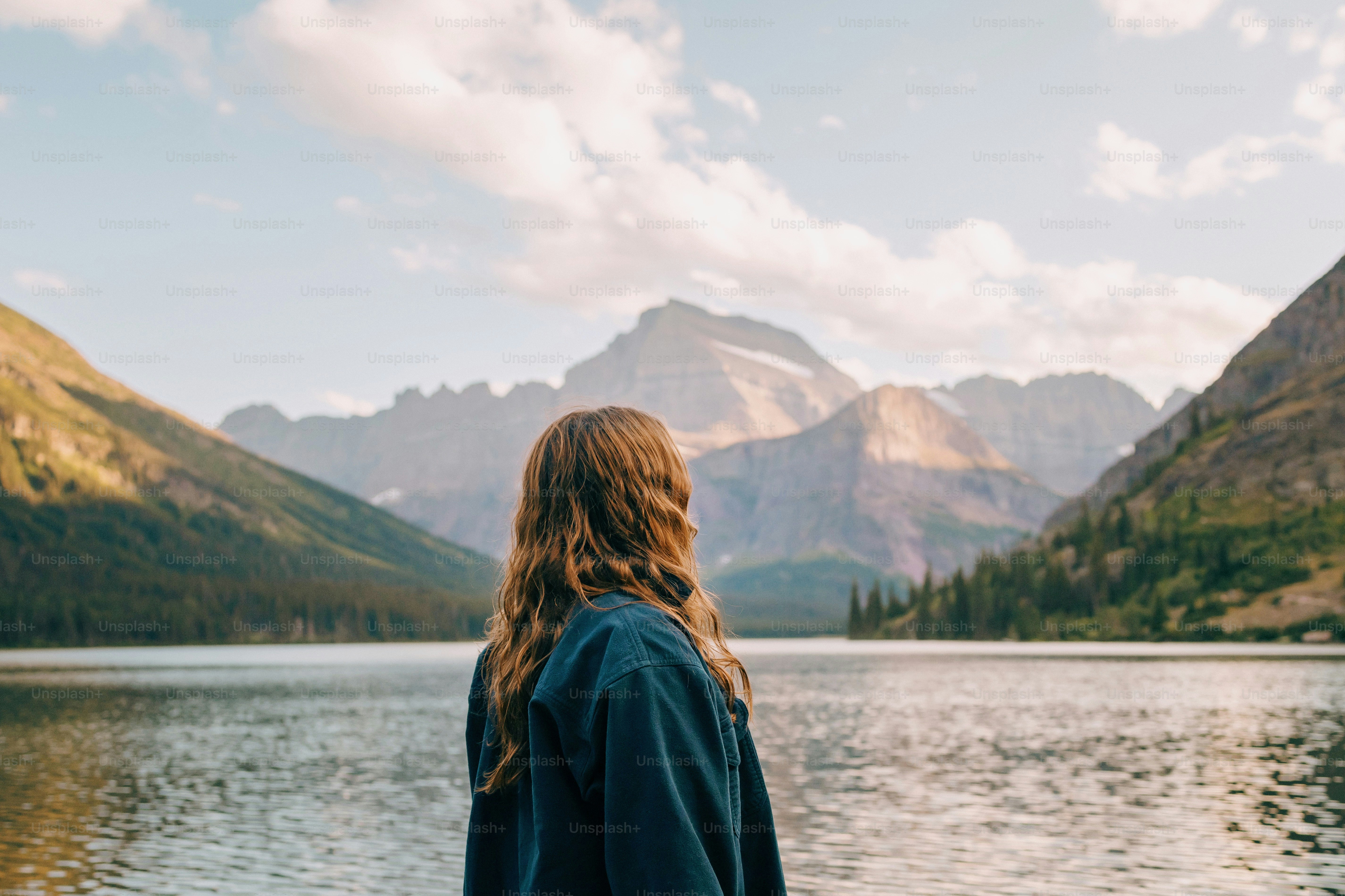 a woman standing in front of a lake with mountains in the background