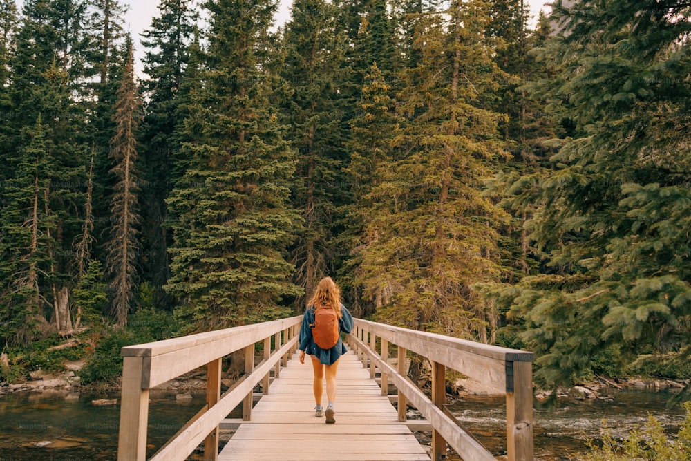 uma mulher caminhando através de uma ponte de madeira sobre um rio