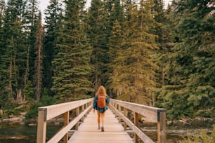 a woman walking across a wooden bridge over a river