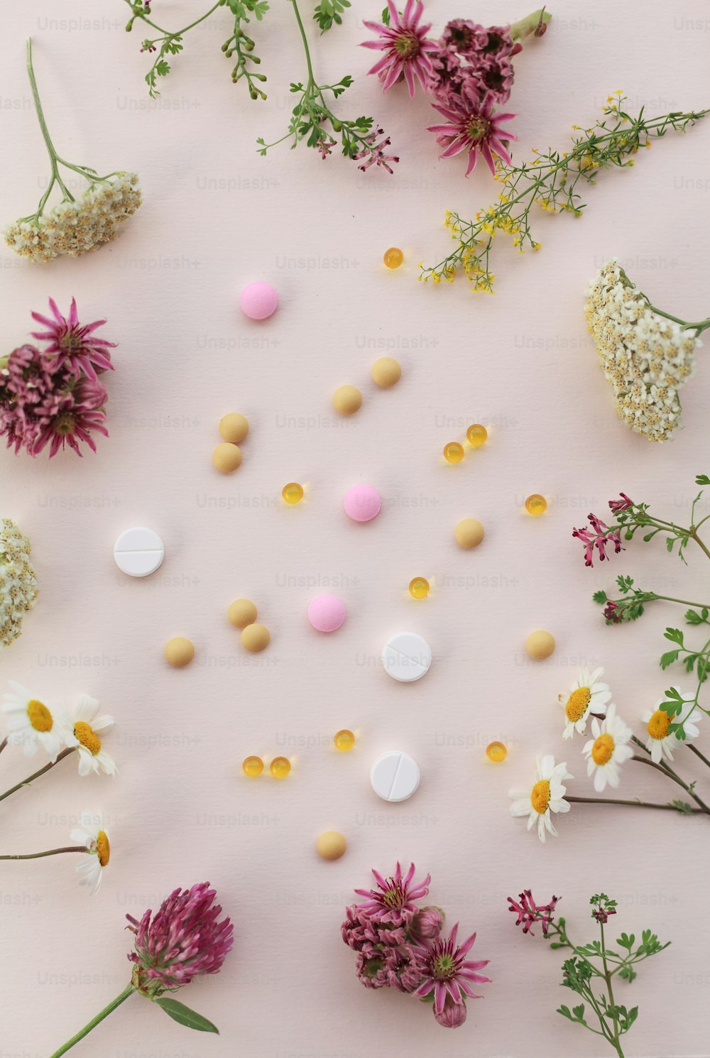 fleurs et pilules disposées en cercle sur une surface rose
