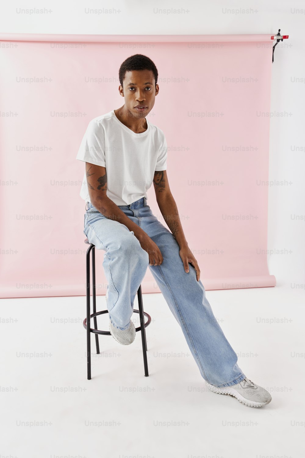 a man sitting on a stool in front of a pink backdrop