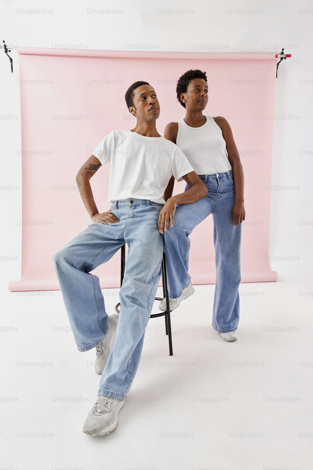 a man and a woman sitting on a chair in front of a pink backdrop